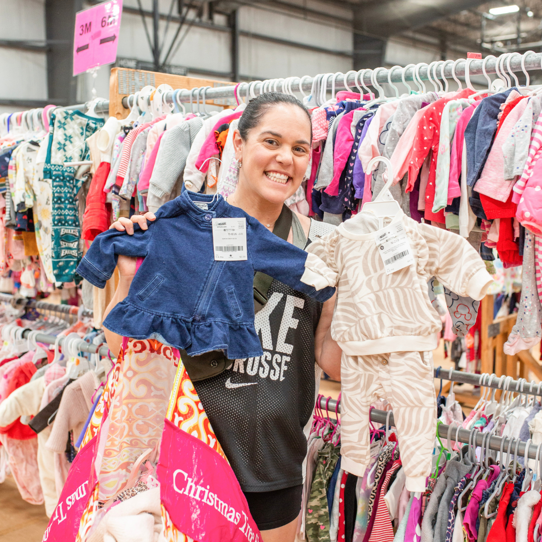 A mom and her child hug in between two rows of little girl clothes