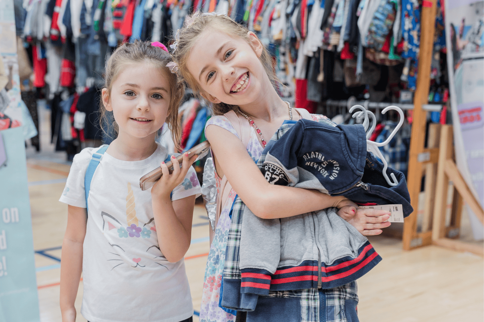 A mom with a large JBF shopping bag on her shoulder stands beside her husband who wears their toddler at a JBF sale.